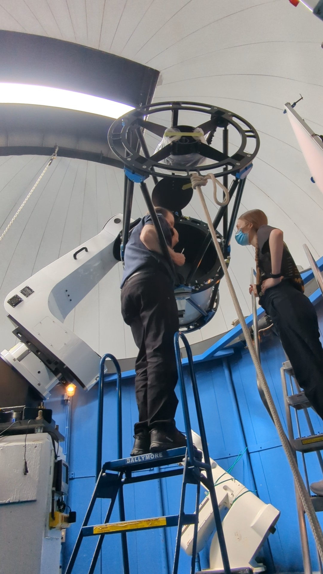 Image from inside the BGO dome, Dave is standing on a ladder with his head inside the telescope, looking at Tiffany standing on the ground.